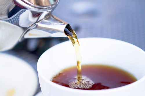 Pouring hot black tea from restaurant style kettle.