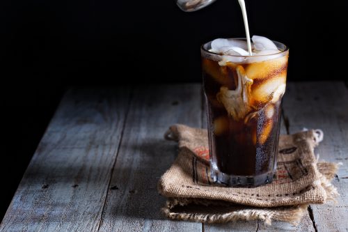 Iced coffee in a tall glass with cream poured over.